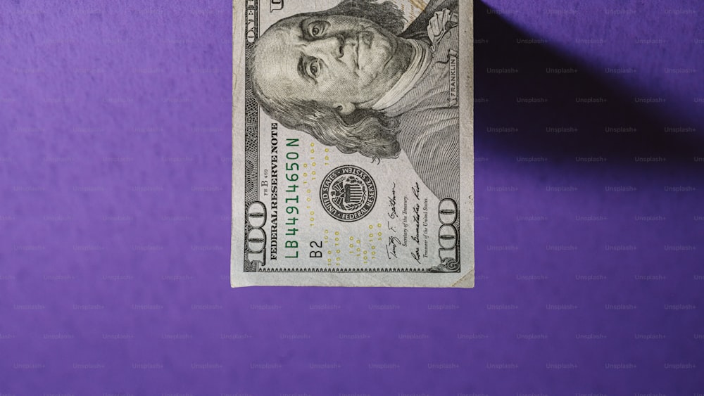 Una banconota da cento dollari che giace su una superficie viola
