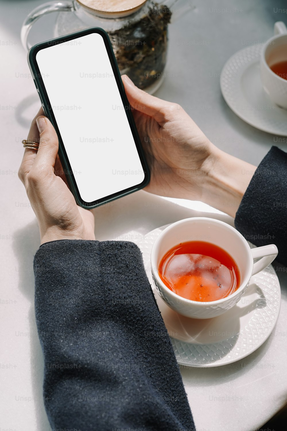 a person holding a smart phone over a cup of tea