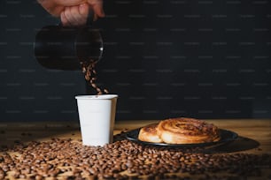 Una persona vertiendo café en una taza sobre un plato de granos de café