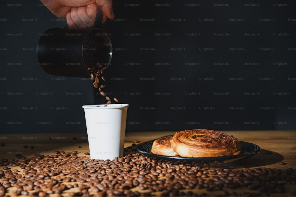 Una persona vertiendo café en una taza sobre un plato de granos de café