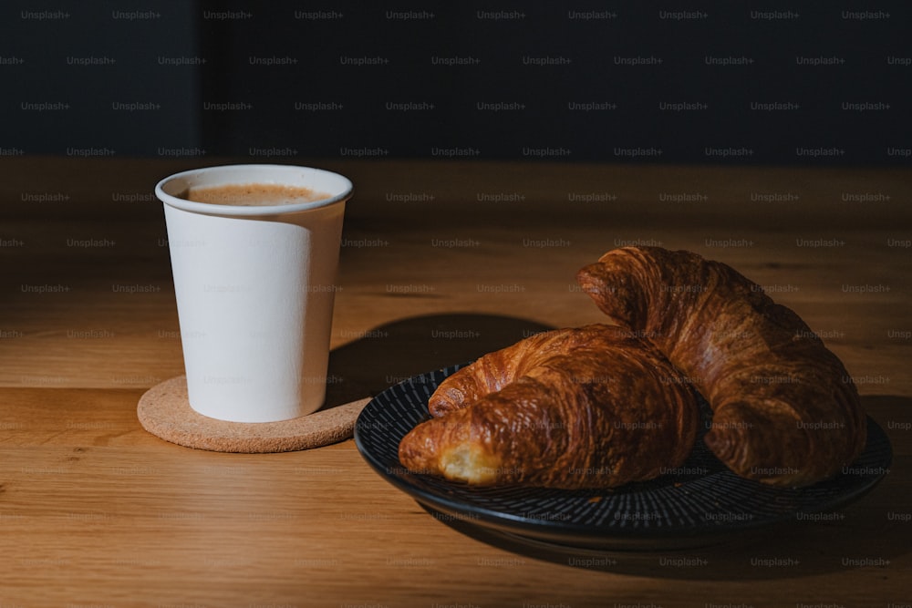 dois croissants em um prato ao lado de uma xícara de café