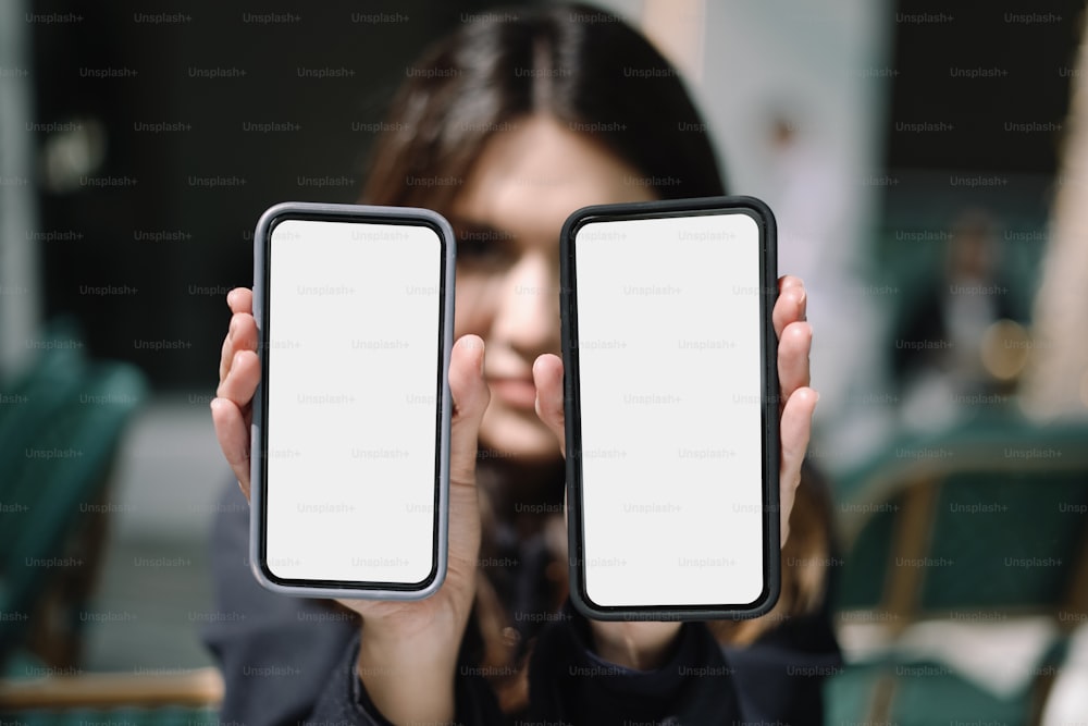 uma mulher segurando dois telefones celulares na frente de seu rosto