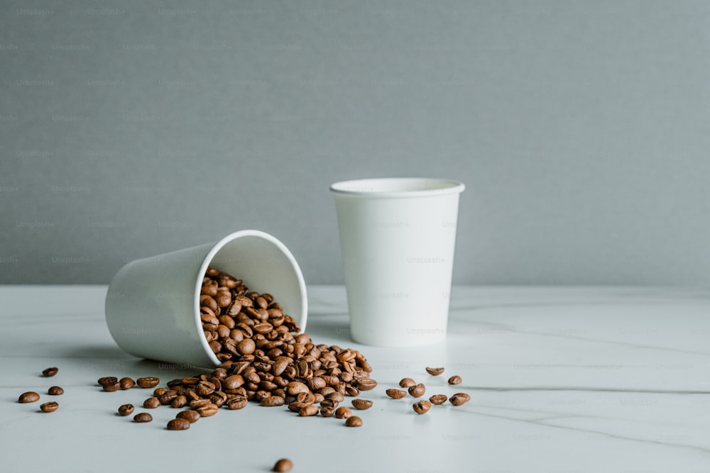 une tasse blanche remplie de grains de café à côté d’une tasse blanche