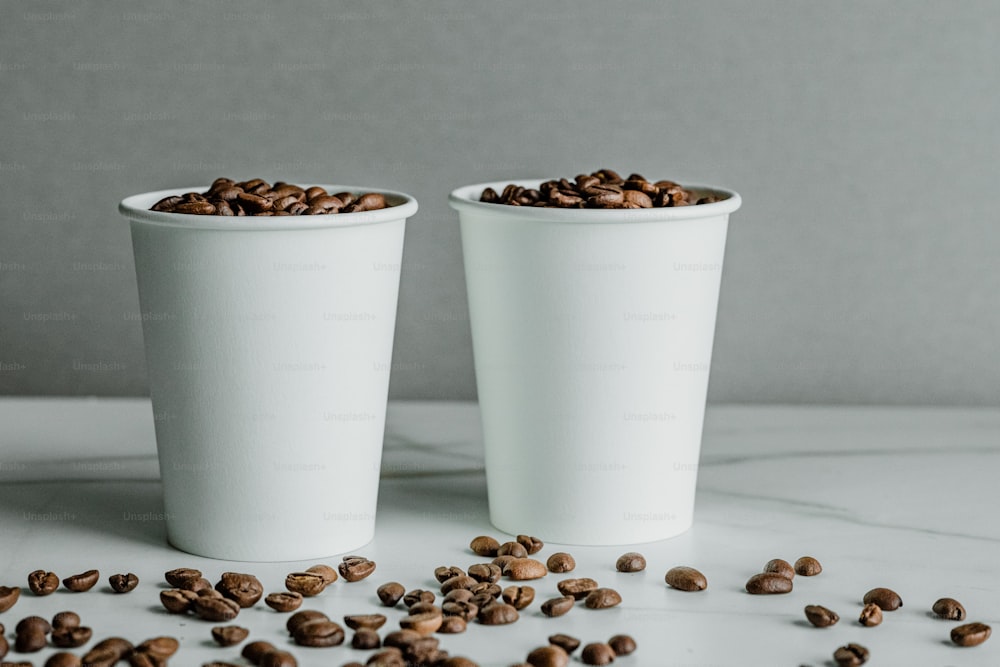 Dos tazas blancas llenas de granos de café sobre una mesa