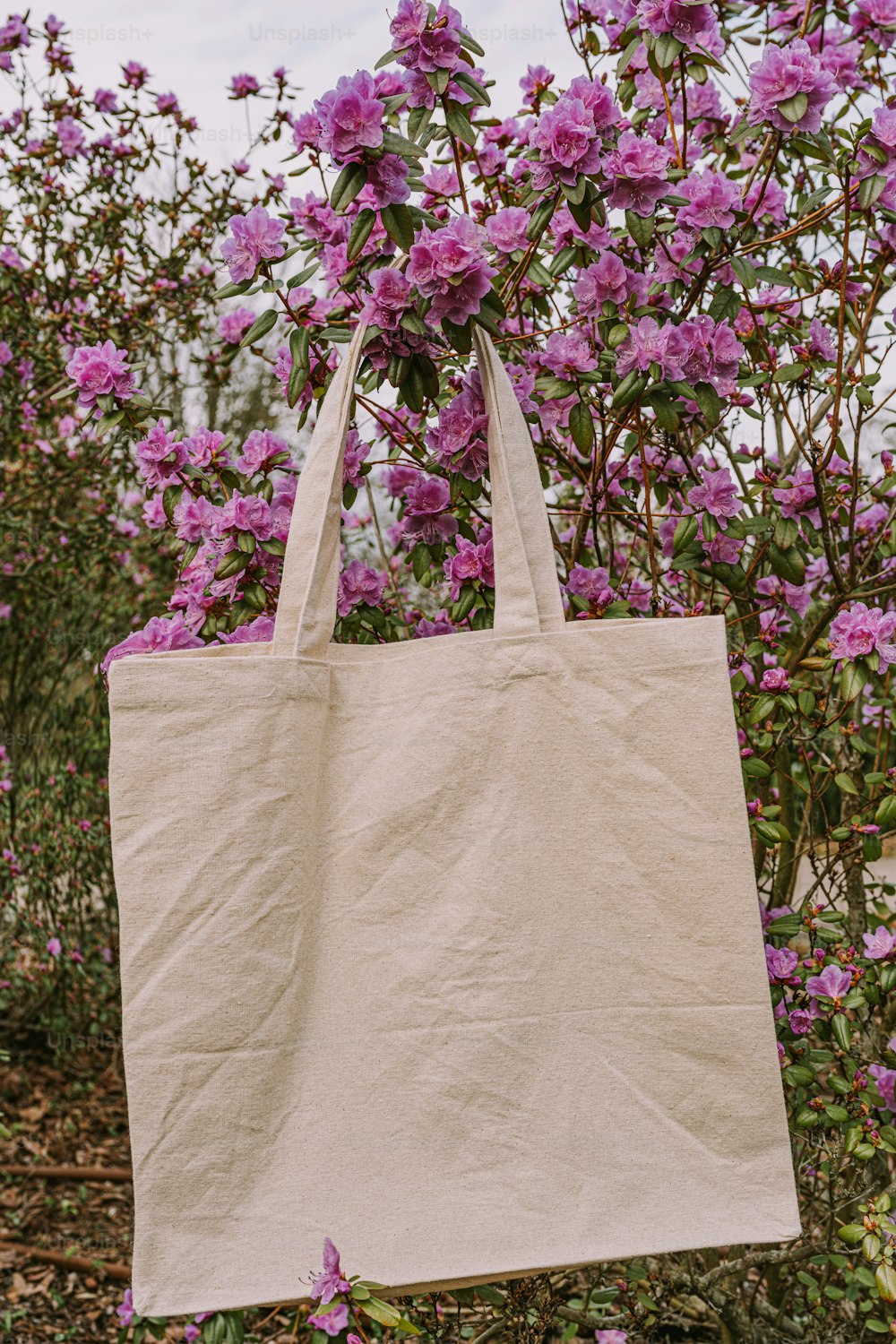 a white bag hanging from a tree filled with purple flowers