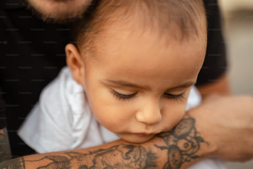 a man holding a baby with tattoos on his arm