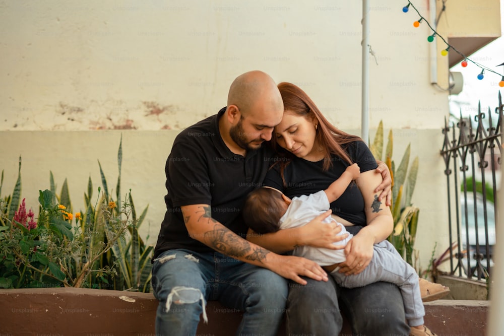 um homem e uma mulher segurando um bebê enquanto estão sentados em um banco