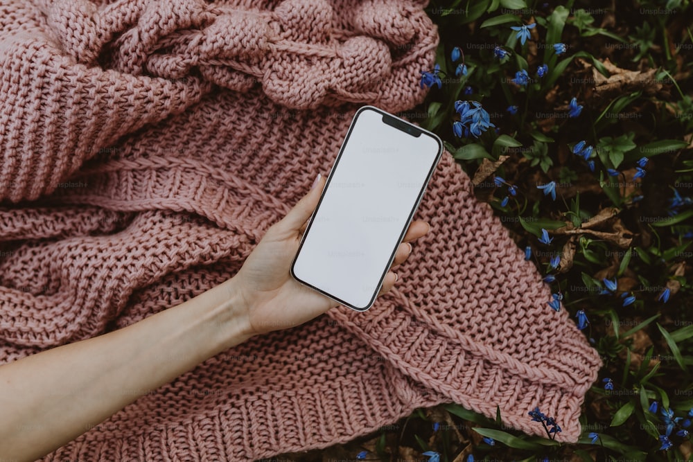 a person holding a cell phone on top of a blanket