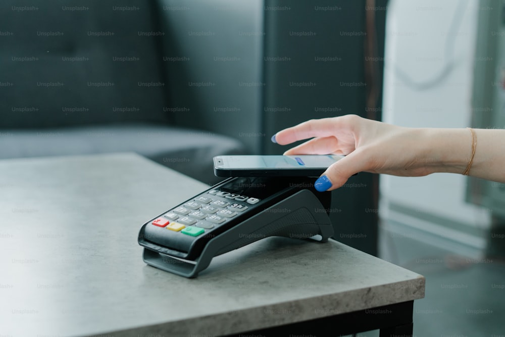a woman's hand holding a cell phone over a cash register