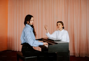 two women sitting at a piano playing a song