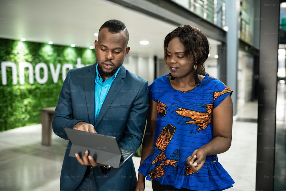 Due giovani imprenditori africani discutono di lavorare insieme su un tablet digitale mentre camminano lungo un corridoio dell'ufficio