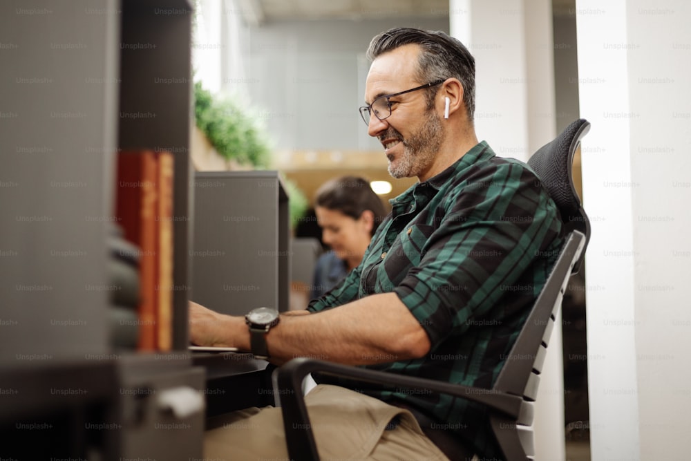 Hombre de negocios sentado en un escritorio privado en el espacio de trabajo de la oficina de coworking, escuchando música mientras trabaja para bloquear el ruido de fondo y las distracciones