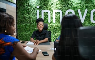 Smiling young African businesswoman talking with colleagues while sitting around a boardroom table