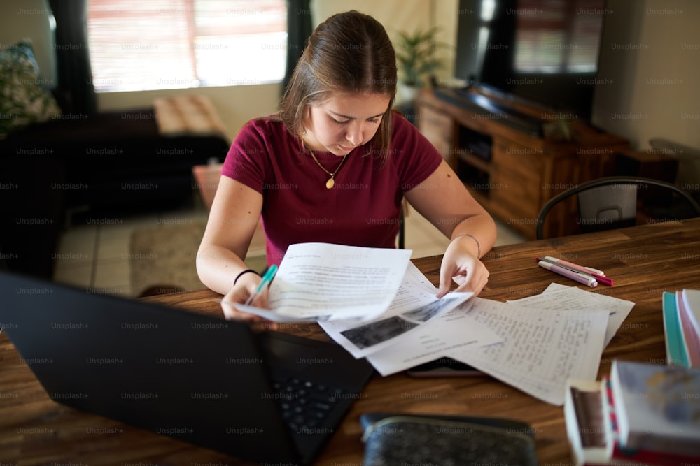 Joven adolescente de escuela revisando notas mientras trabaja desde casa debido a la pandemia mundial.