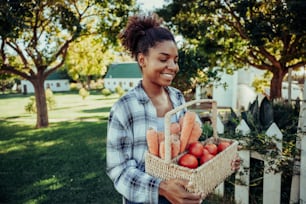 Mujer de raza mixta caminando por el pueblo agrícola llevando una canasta fresca de verduras sonriendo en el cálido día de verano. Foto de alta calidad