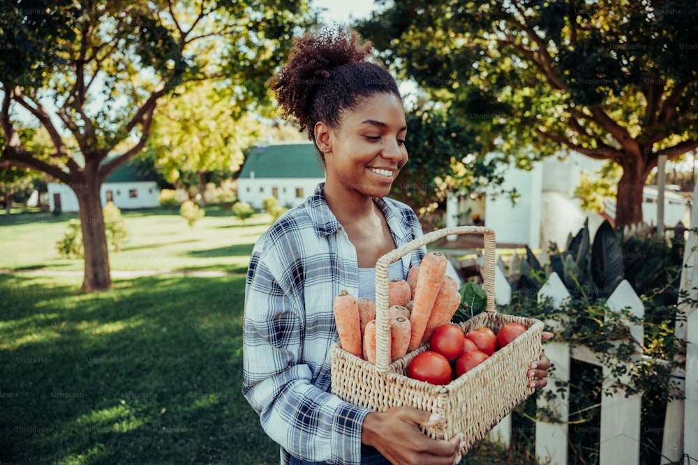 Mixed race female walking through farm village carrying fresh basket of vegetables smiling on warm summers day. High quality photo