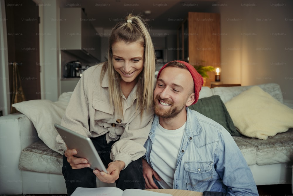 Couple heureux de race blanche travaillant à domicile à l’aide d’une tablette numérique assis sur un canapé. Photo de haute qualité