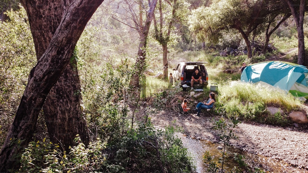 a group of people sitting around a tent in the woods