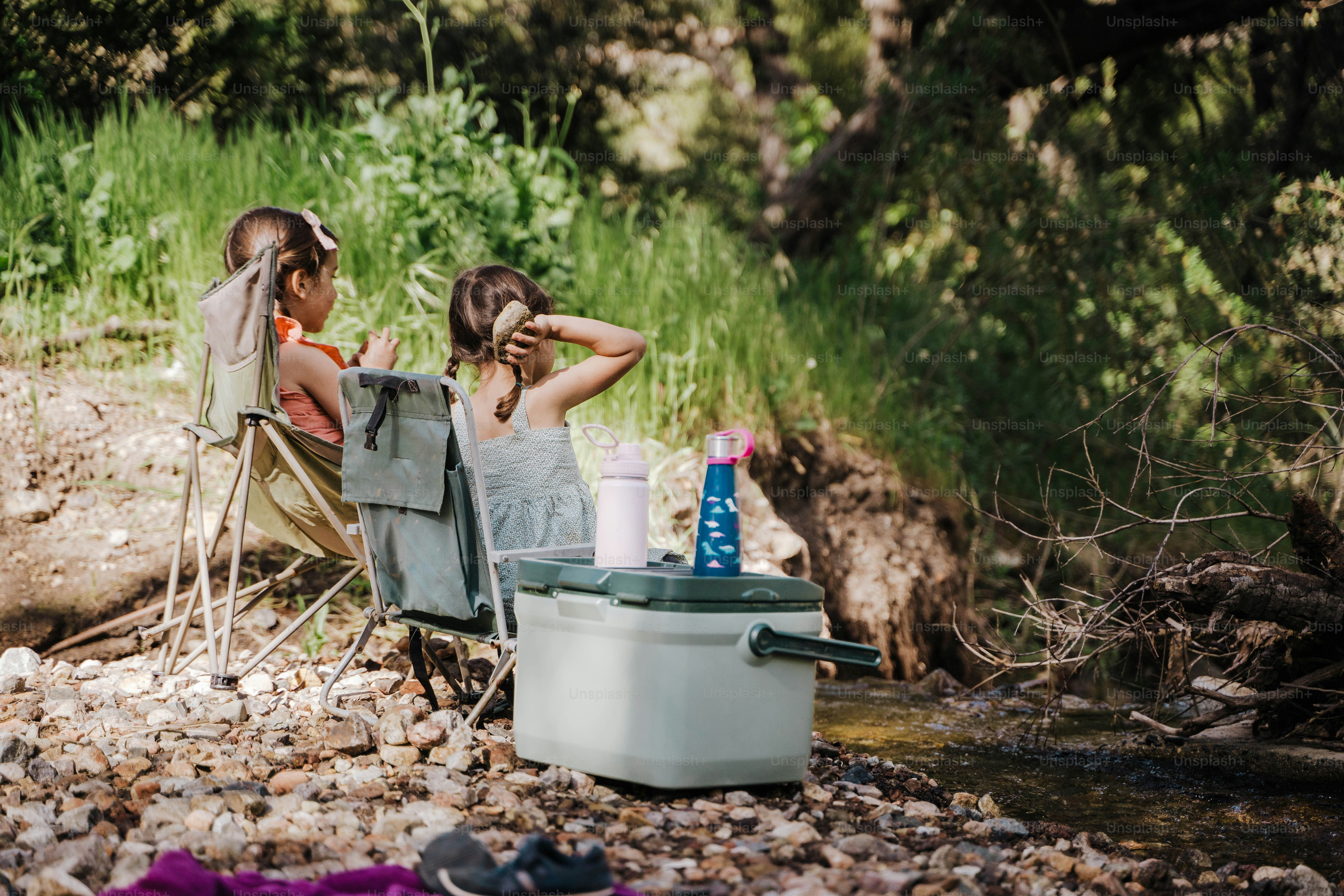 A couple of people sitting in chairs next to a river photo – Family ...