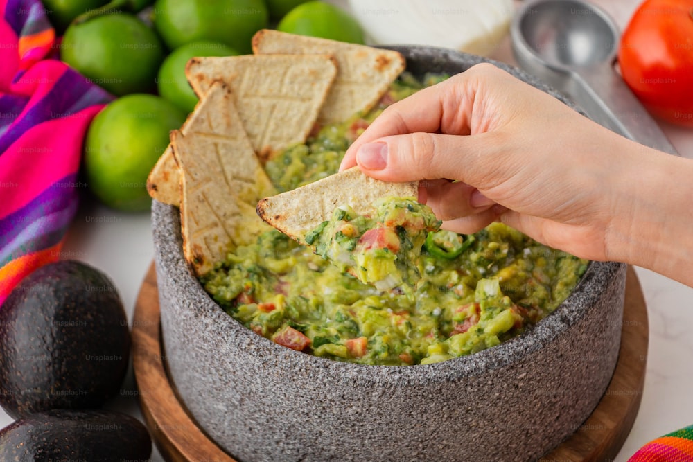 a hand dipping a tortilla chip into a bowl of guacamole