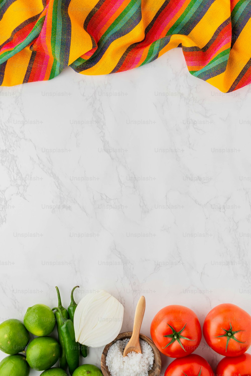 a marble counter top with tomatoes, limes, garlic, and a towel