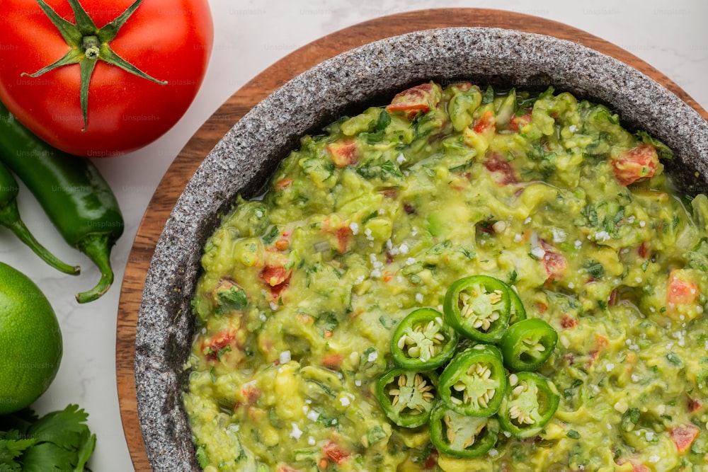 a bowl filled with guacamole next to tomatoes and green peppers