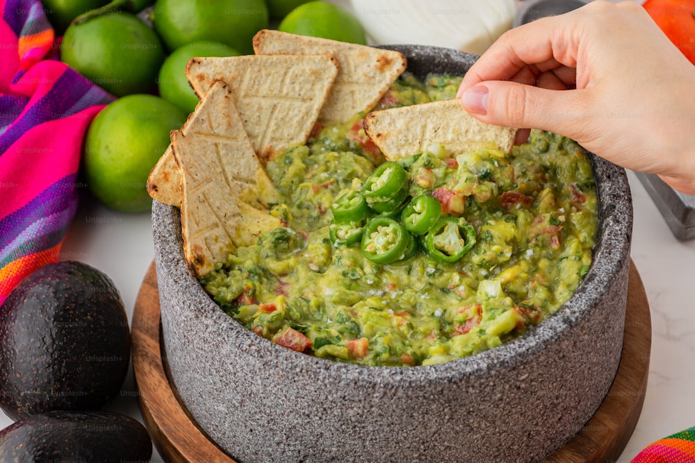 a person dipping a tortilla chip into a bowl of guacamole