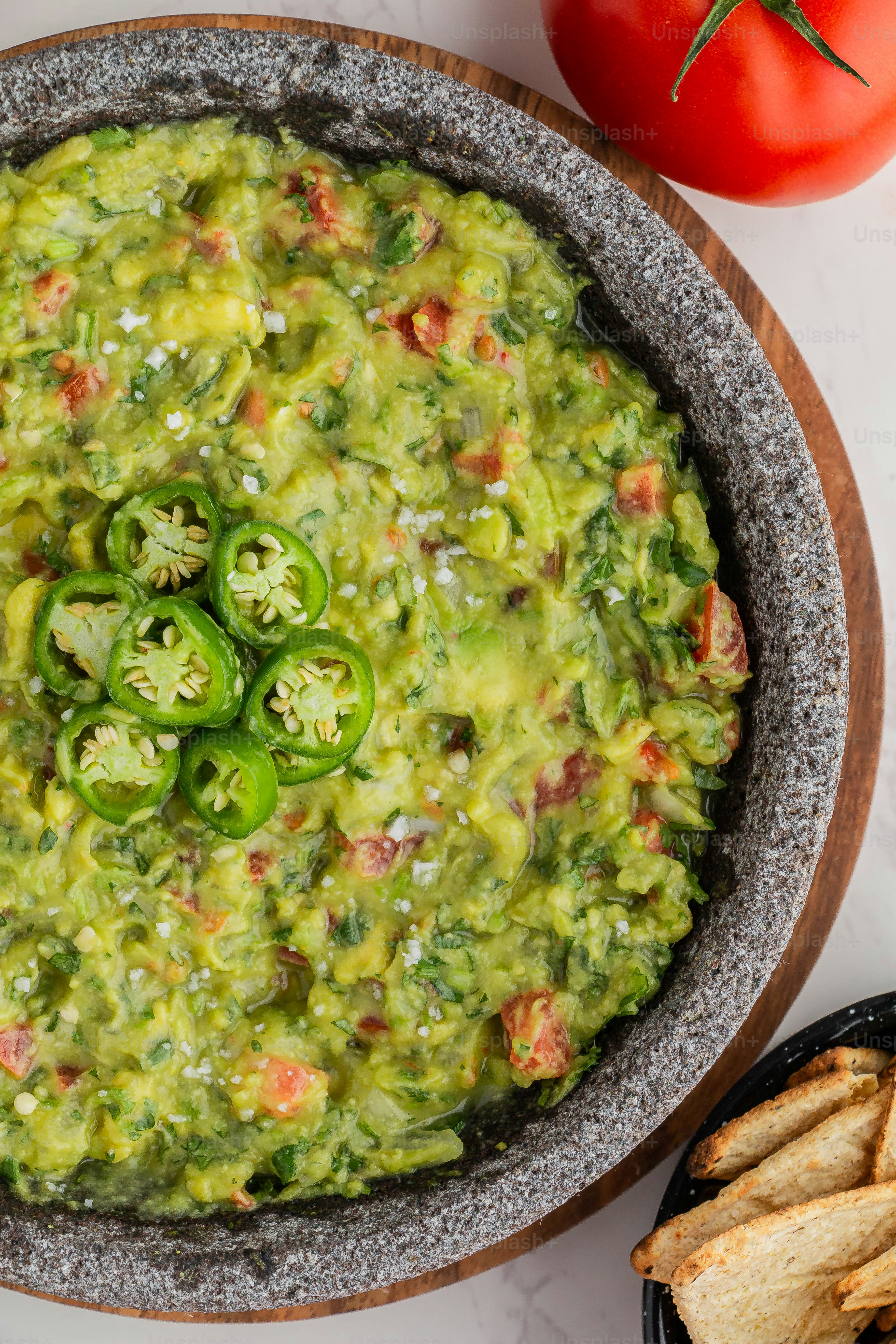 a bowl of guacamole next to some chips and a tomato