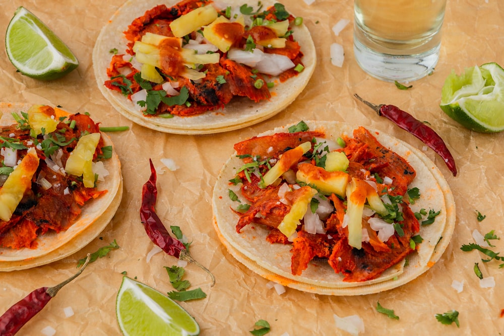 three tortillas with meat and vegetables on a table next to a glass of