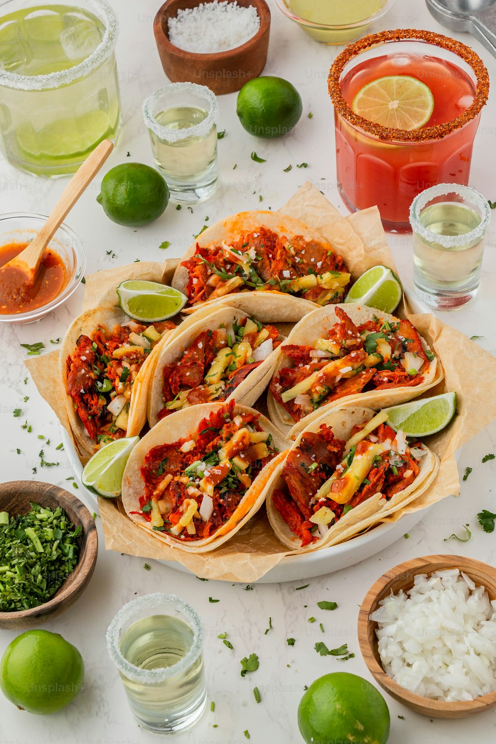 a table topped with tacos and limes next to drinks