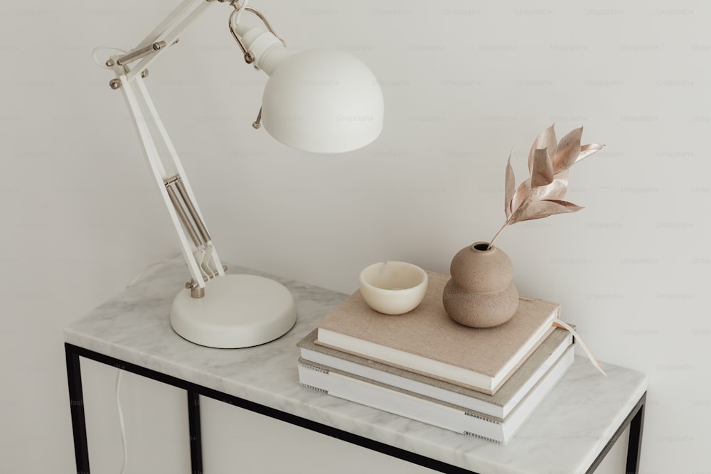 uma mesa com uma lâmpada, livros e um vaso sobre ela