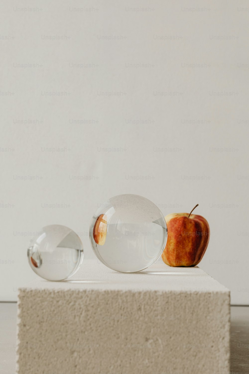 una mela e due palline di vetro su una superficie bianca
