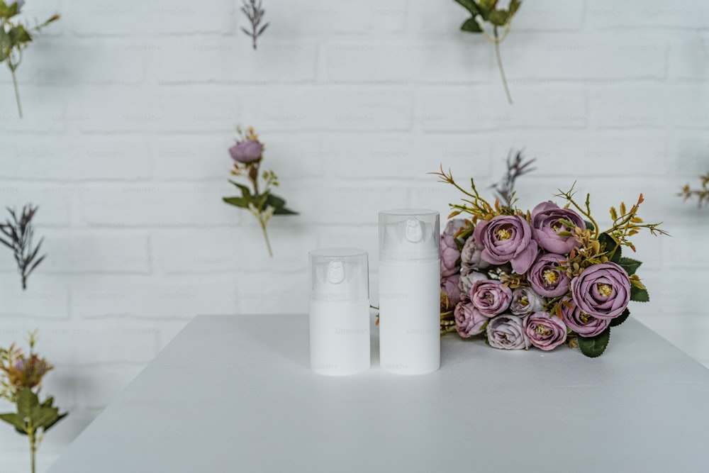 a white table topped with two bottles of lotion next to a bouquet of flowers