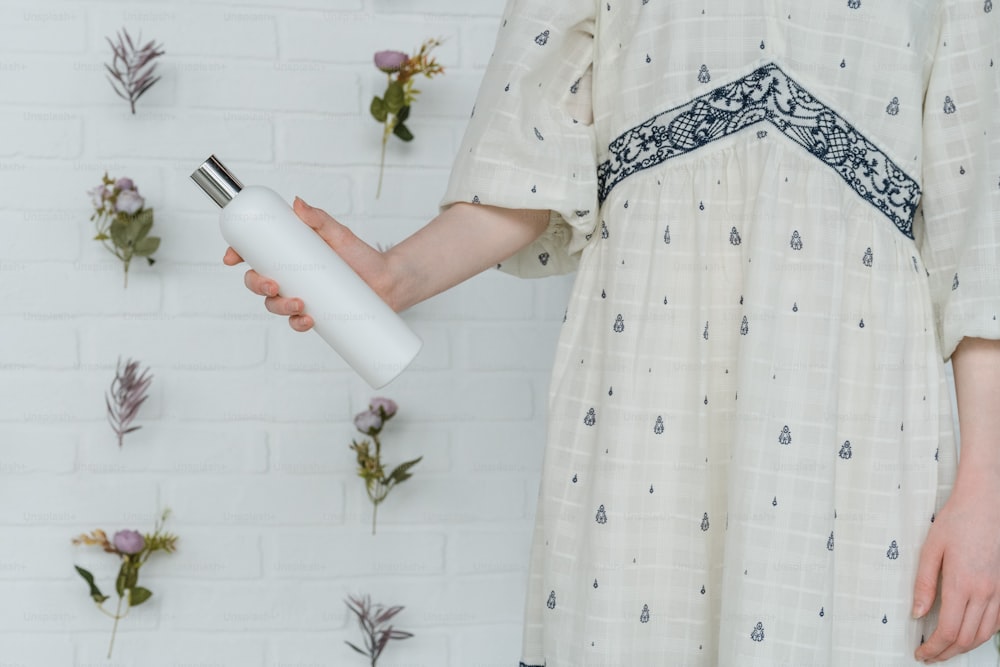 una donna in un vestito bianco che tiene una bottiglia bianca