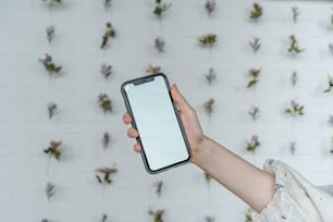 a person holding a cell phone in front of a wall of flowers