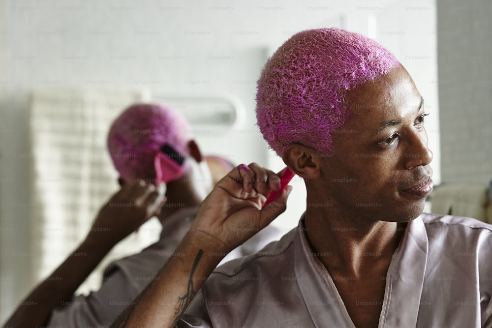 Ein Mann mit einer rosa Frisur föhnt sich die Haare