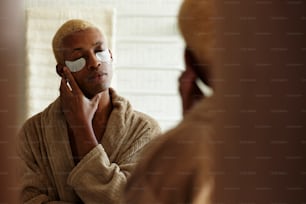 목욕 가운을 입은 남자가 거울에 비친 자신의 모습을 보고 있다