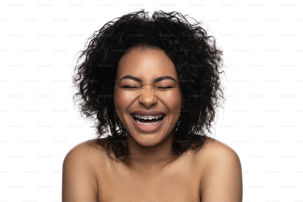 흰색 배경에 대해 치아에 교정기를 착용한 행복한 미소 짓는 흑인 여성