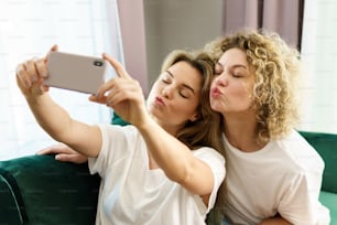 Two young and cheerful girls taking selfie together at home