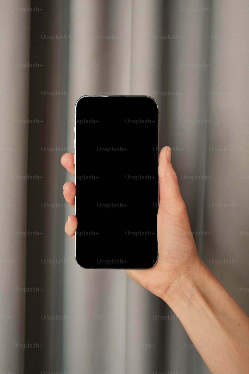 a hand holding a black cell phone in front of a curtain