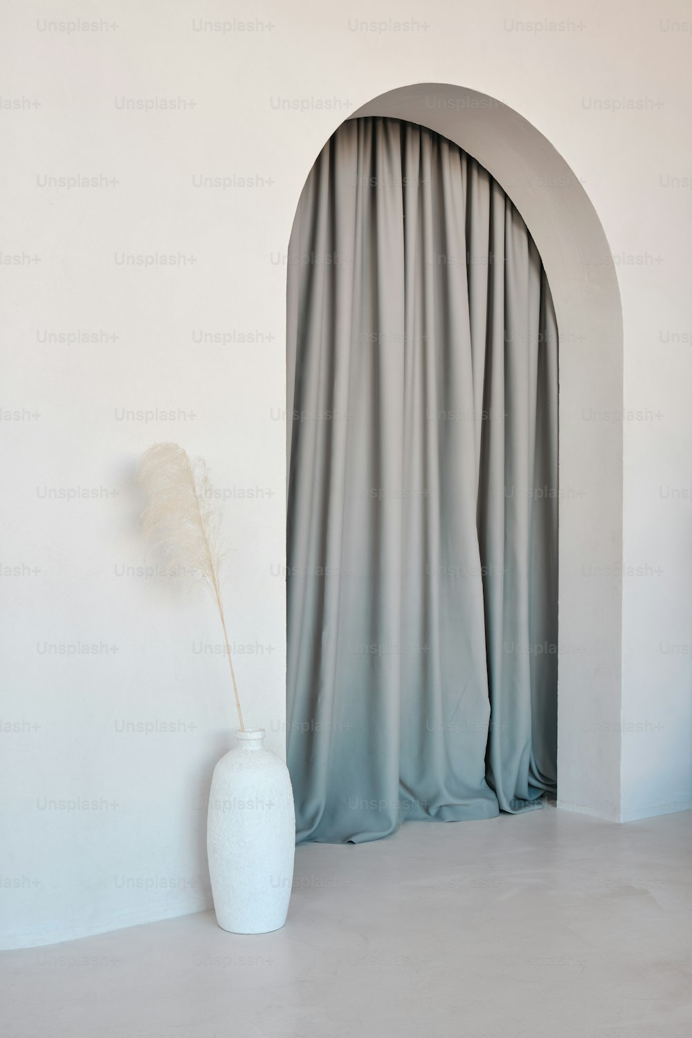 a white vase sitting in front of a curtain