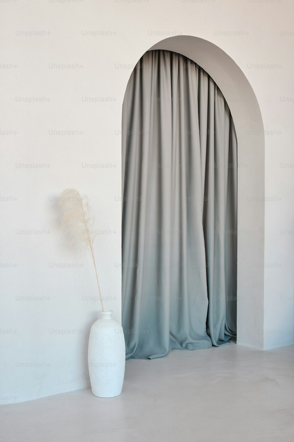 a white vase sitting in front of a curtain