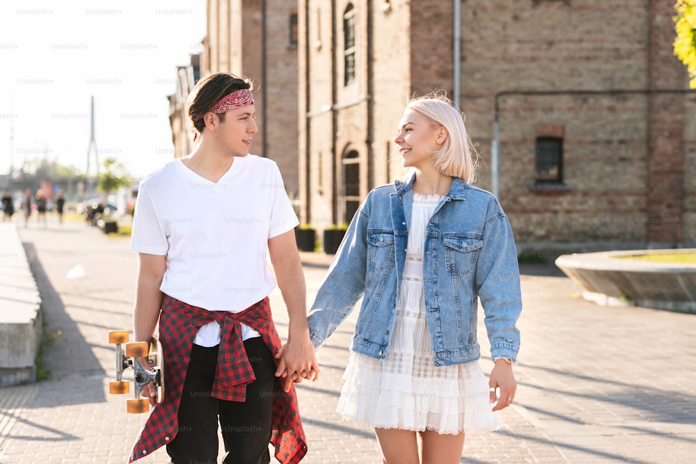 Stilvolles Teenager-Paar mit einem Longboard während ihres Dates in einer Stadt