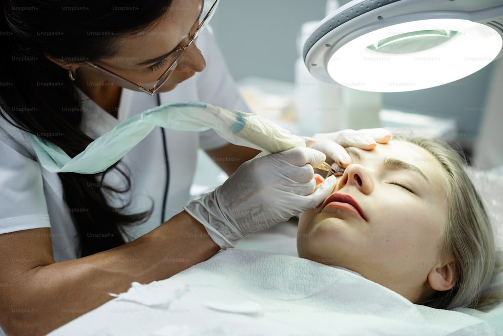 Make-up artist permanente professionista e la sua cliente durante il trattamento di miglioramento della linea delle ciglia