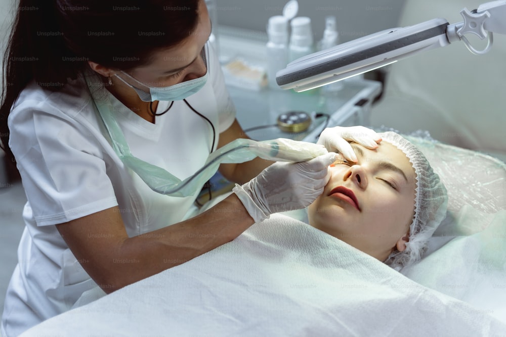 Make-up artist permanente professionista e la sua cliente durante il trattamento di miglioramento della linea delle ciglia