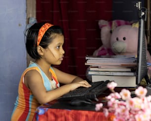 una niña india con rostro intenso asistiendo a clase en línea en una computadora de escritorio durante el brote de pandemia de COVID-19