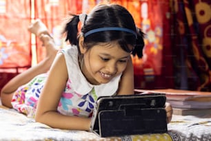 an Indian girl child with smiling face attending online class on tablet during COVID-19 pandemic outbreak