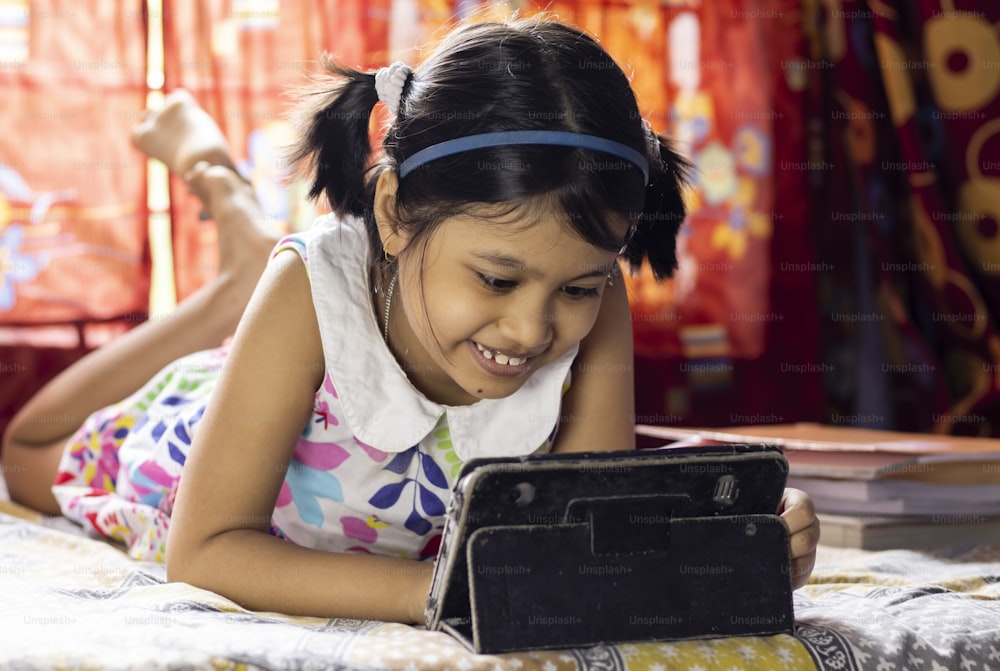 COVID-19 전염병 발생 기간 동안 태블릿으로 온라인 수업에 참석하는 웃는 얼굴을 가진 인도 소녀