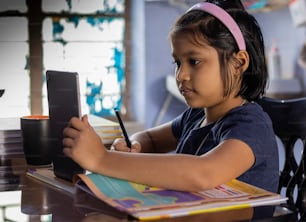 una bambina sveglia indiana che studia a casa con il tablet