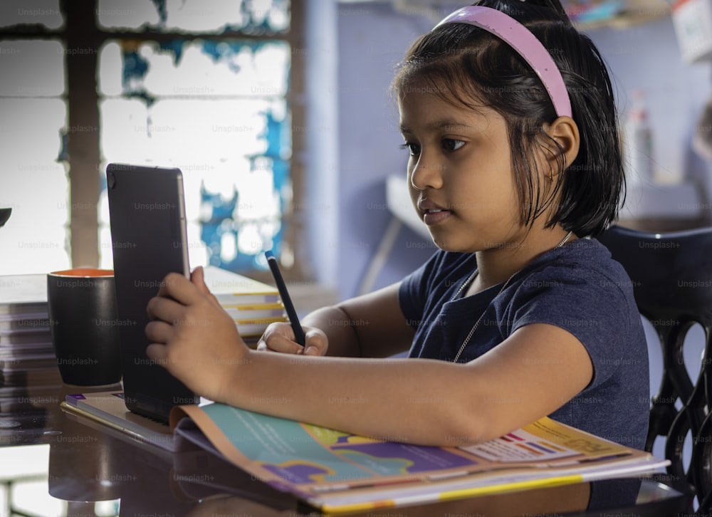 an Indian cute girl child studying at home with tablet
